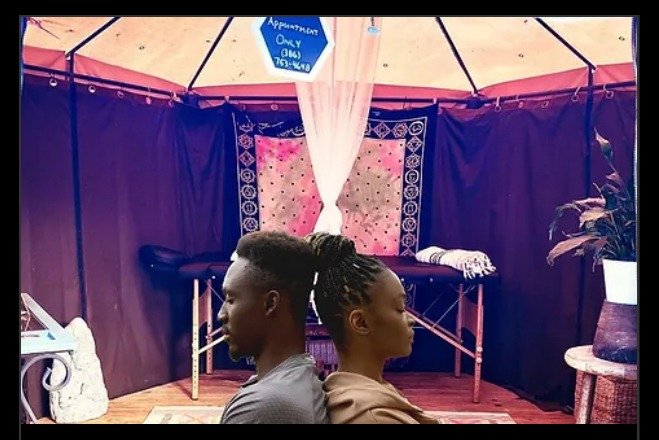 A couple sitting back-to-back in meditation inside a holistic massage therapy tent.